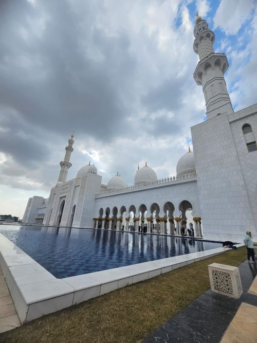 Sheikh Zayed Grand Mosque Courtyard, Grand Mosque Exterior at Sunset, Chandelier in the Main Prayer Hall, World's Largest Hand-Knotted Carpet, Intricate Column Design, Reflective Pools at Night, Visitors in the Mosque's Courtyard, Guided Tour in Progress, Aerial View of the Mosque, Women in Traditional Abayas